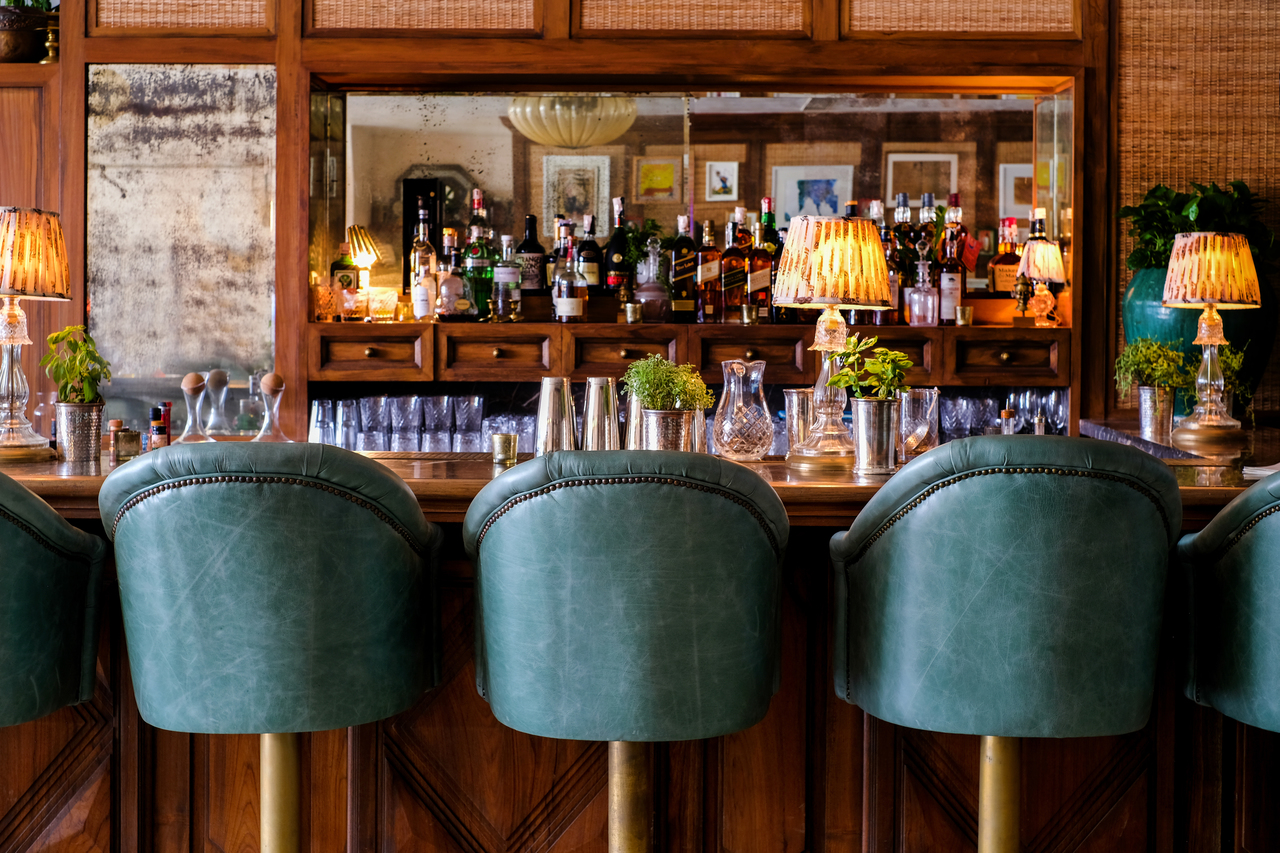 Three leather stools in front of a stocked wooden bar